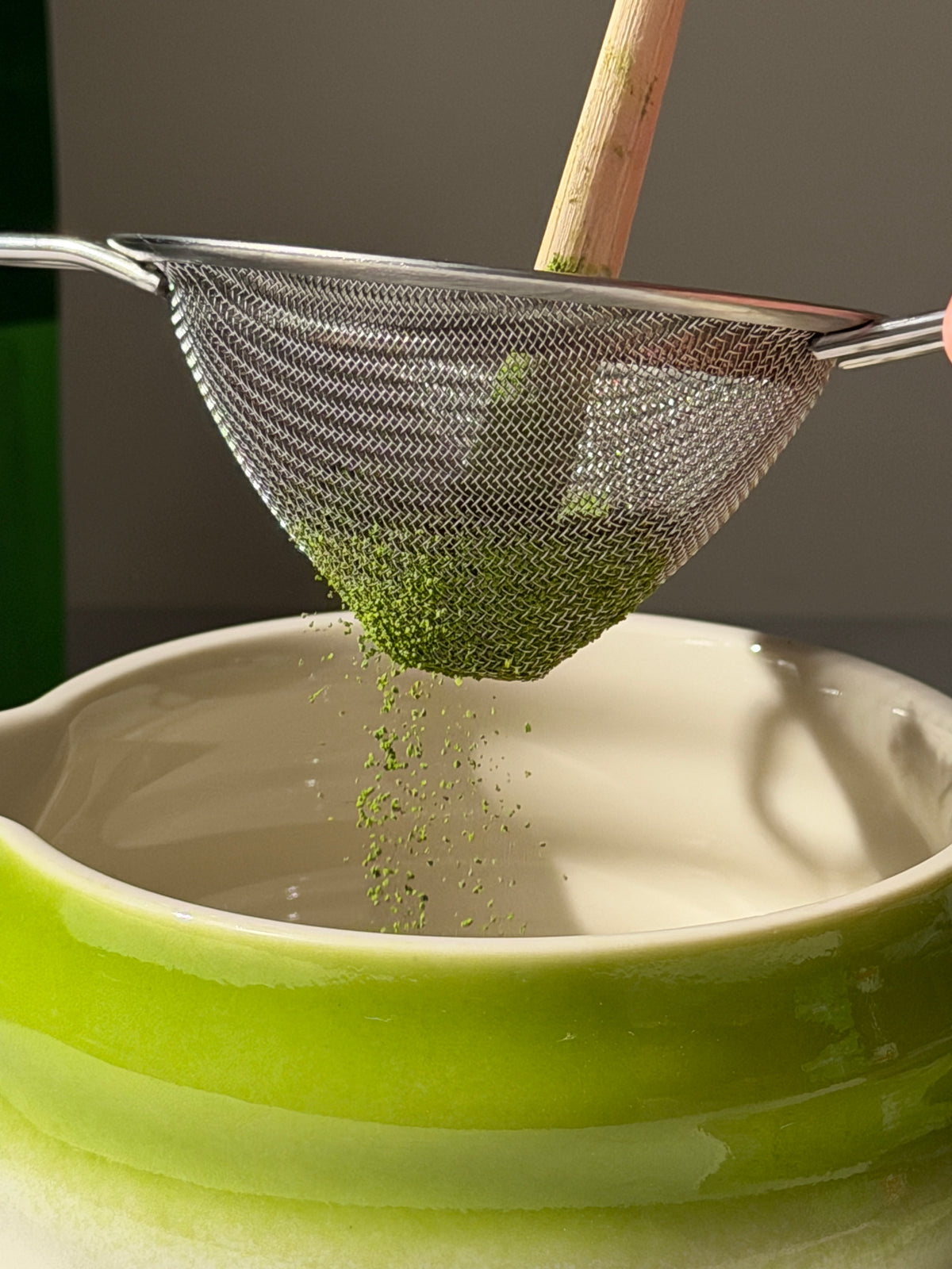 a hand holding a sieve over a green bowl
