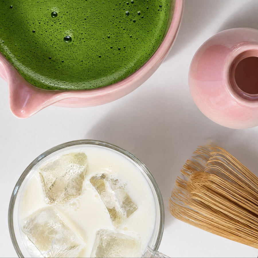 a green drink in a glass cup next to a whisk and a jar